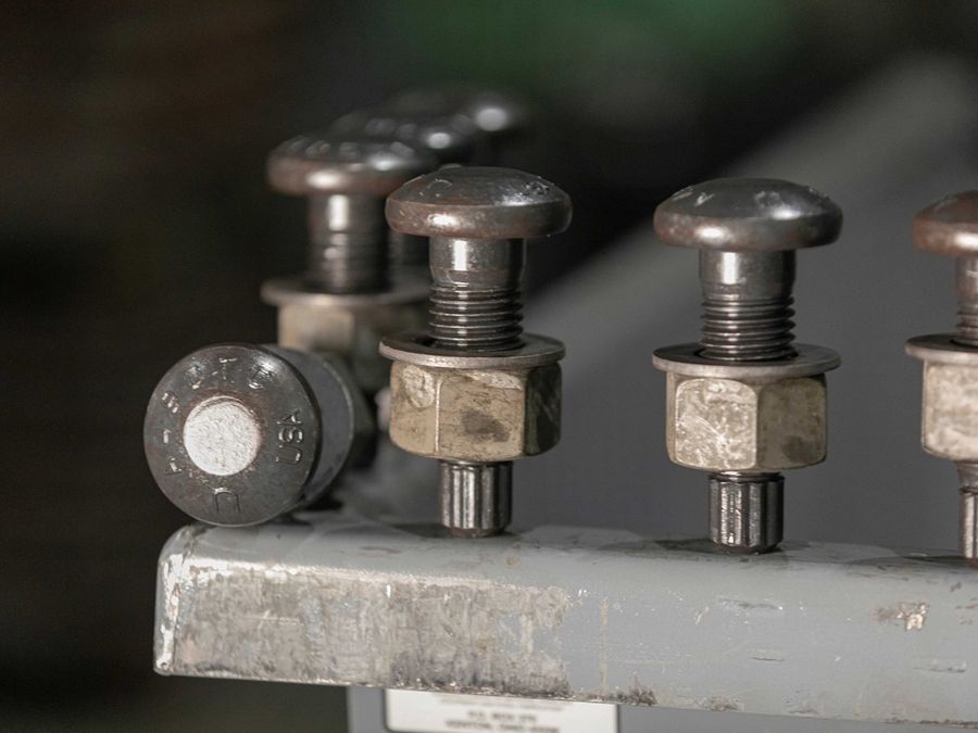 Heavy structural bolts with nuts and washers lined up on a steel edge